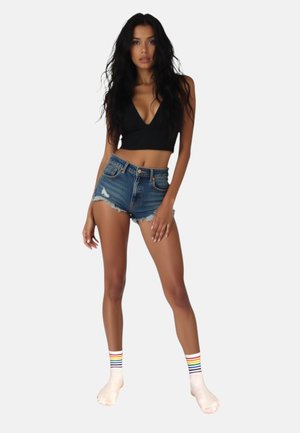 Sort cropped top, slidte denim shorts og cremede sokker med regnbue-striber. Fokus på teksturer og farvekontraster.