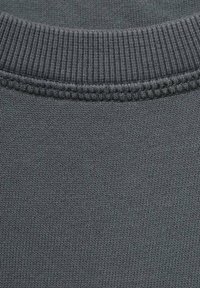Tessuto grigio scuro con una fine texture a costine e una cucitura del collo liscia. Decorazioni cucite mettono in risalto i bordi dell'indumento.