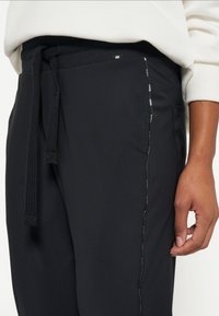 Schwarze Sporthosen mit einem strukturierten elastischen Bund, verstellbarem Kordelzug und seitlicher Tasche mit reflektierendem Dekor.