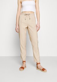 Beige lätta byxor med dragsko i midjan och veck. Styld med bruna sandaletter med remmar och vävd sula.