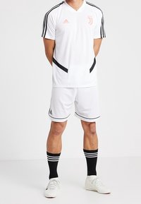 Vitt sportset bestående av en kortärmad tröja med svarta detaljer och tre ränder, matchande shorts och knälånga svarta strumpor.