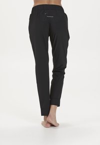 Svarta sportbyxor med elastisk midja, med en bakficka och avsmalnande ben; slät textur med en elegant, åtsittande design.