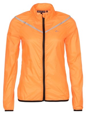 Žena v jasně oranžové bundě na zip, černém sportovním podprsence, černých krátkých legínách a černých běžeckých botách v polovičním kroku.