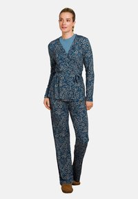Blauwe bloemenpatroon wikkeltop en bijpassende broek, gemaakt van zachte stof met lange mouwen en een striktaille. Gecombineerd met bruine slippers.