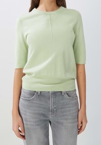Pull en maille courte à manches courtes de couleur vert clair, doté d'un col rond et d'un ourlet côtelé, associé à un jean en denim gris.