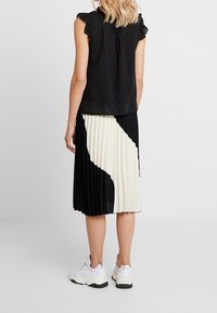 Černý top s volánovými rukávy doplněný plisovanou sukní s černo-bílým abstraktním vzorem. Nosené s bílými sportovními botami.