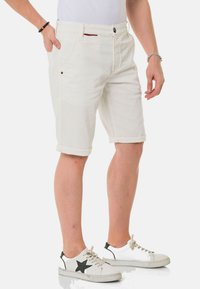 Shorts en denim blancs avec des ourlets retournés, poches avant, une poche arrière et une fermeture à bouton. Associés à des baskets blanches avec des accents noirs.