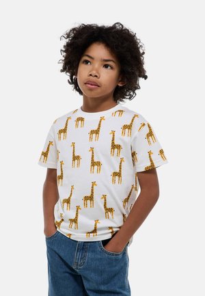 T-shirt en coton blanc avec un motif de girafe intégral en orange et noir. Manches courtes, col rond, coupe décontractée, associé à un short en jean.