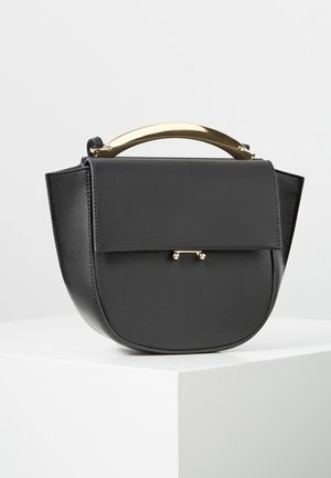 Bolso de mano de cuero negro con forma curva, cierre de solapa y asa dorada brillante apoyado sobre un pedestal blanco contra un fondo neutro.