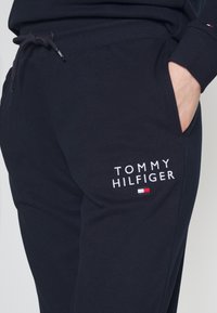 Pantaloni della tuta blu navy realizzati in misto cotone, con logo ricamato "TOMMY HILFIGER" e un piccolo accento rosso, bianco e blu vicino alla tasca.
