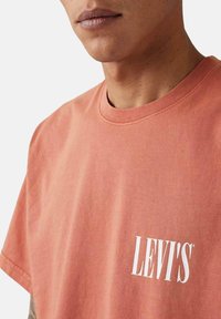 Camiseta de algodón rosa con mangas cortas, que presenta un logotipo blanco de "LEVI'S" en la parte delantera, cuello redondo y corte relajado.