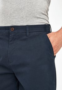 Chino navy con una texture liscia, dotati di un bottone marrone, tasche standard e una cintura slim. Design casual adatto per l'uso quotidiano.