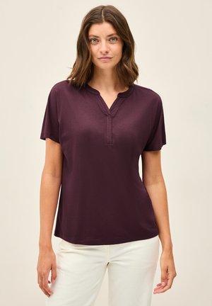 Kortærmet, mørklilla top med en afslappet pasform, der har en delvis knaplukning og en glat overflade, parret med lyse pants.