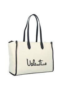 Canvas tote bag in cream with black leather straps. Features a prominent black logo, zip closure, and a rectangular shape.