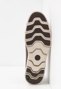 Brun gummisul med ett texturerat grått mönster, med djupa spår för grepp och en logotyp i mitten.