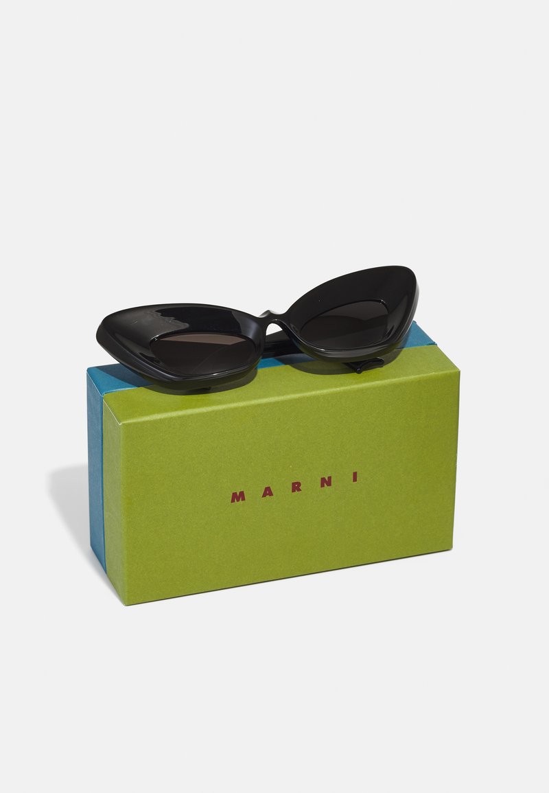 Black cat-eye sunglasses resting on a green and blue box labeled "MARNI." The glasses have a glossy finish and distinct shape.