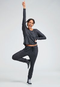 Black, sparkly loungewear set featuring a loose-fitting long-sleeve top and drawstring pants. Model poses playfully in black sneakers.