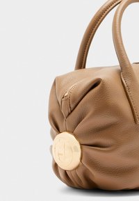 Sac à main en cuir marron avec une forme arrondie, doté d'un bouton logo doré et d'une petite fermeture éclair. La texture semble douce et souple.