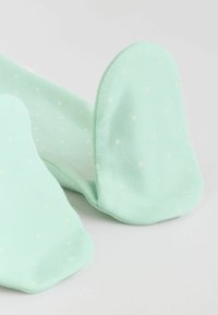 Pehmed piparmündirohelised beebisokid väikeste valgete täpikestega, paljastades talla ja varvaste osa heledal taustal.