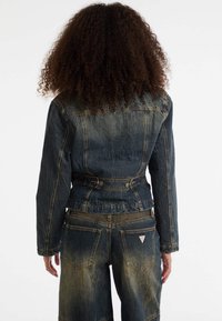 Giacca di jeans con vita aderente, leggero sbiadimento, dettagli con bottoni e cuciture, abbinata a jeans a gamba larga con tasche posteriori.