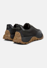 Black slip-on sneakers with textured rubber and mesh upper, rounded toe, and a durable, patterned gum sole. Features subtle branding on the heel.