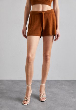 Brune strikkede shorts med knytteliv, parret med strappy hvite høyhælte sandaler. Glatt tekstur, over-kne-lengde.