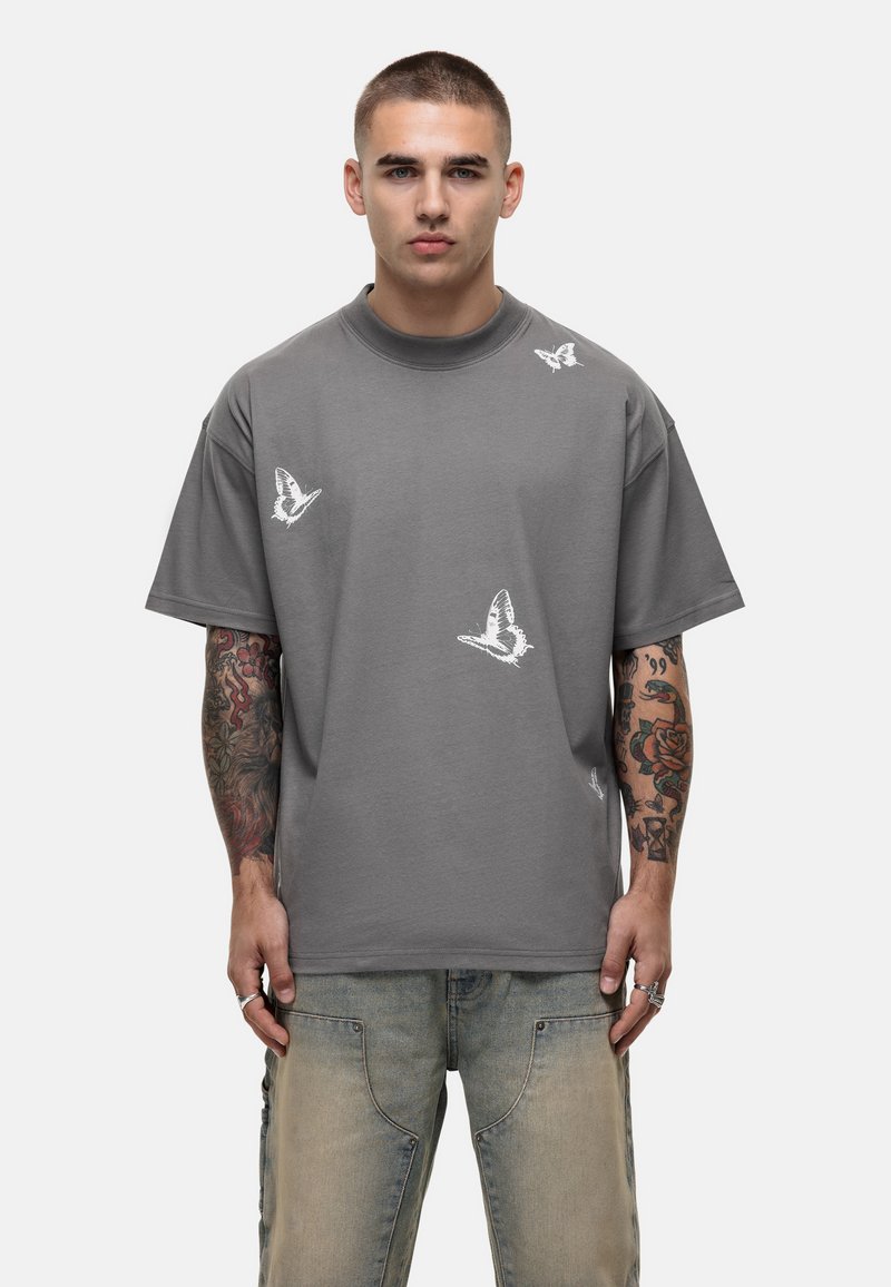 Grijze katoenen t-shirt met korte mouwen, voorzien van witte vlinderprints verspreid op de voorkant. Ronde hals met een relaxte pasvorm.