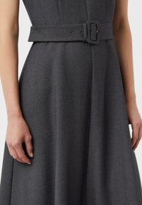 Szara sukienka wykonana z fakturowanej tkaniny, z dopasowanym gorsetem, szerokim paskiem z prostokątną klamrą oraz rozszerzaną, swobodnie opadającą spódnicą.