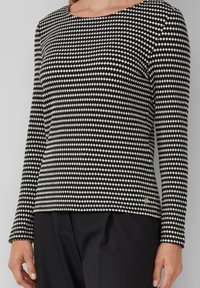 Czarny i biały longsleeve wzorzysty top z małymi diamentowymi kształtami, noszony z czarnymi spodniami, pokazujący tors i ręce na jednolitym tle.