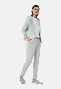 Hellegrau gefütterte Kapuzenjacke, weißes Oberteil, hellgraue tapered Hose und schillernde silberne Ballettschuhe. Glattes Material mit minimalen Details.
