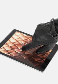 Zwarte leren handschoen raakt een tablet scherm aan met een textuur van een bruine achtergrond waarop het logo "PEARLWOOD" en een naald graphic te zien zijn.