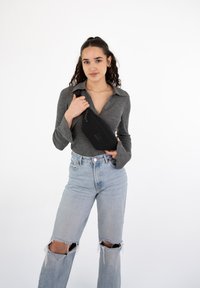 Marsupio nero appoggiato su una maglietta grigia a maniche lunghe. Jeans in denim azzurro chiaro a vita alta con strappi e buchi sulle ginocchia.