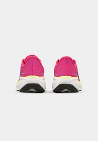 Pink mesh running shoes with a white sole and textured black outsole. Features yellow accents and reflective hardware near the heel.