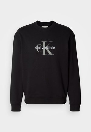 Black long-sleeve sweatshirt with ribbed cuffs and hem, featuring grey and white Calvin Klein "cK" logo centered on the chest.