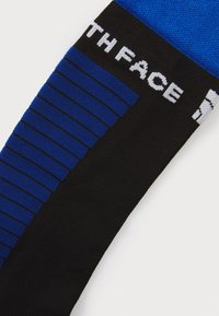 Crne i plave čarape s prugastim dizajnom u plavoj boji, teksturiranim gornjim dijelom i bijelim logotipom "THE NORTH FACE" sa strane.