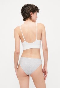 Hvit bomullsbralette med tynne stropper og en grå bomullsbikini-bunn. Begge har enkle design, som fremhever glatte teksturer og nøytrale farger.