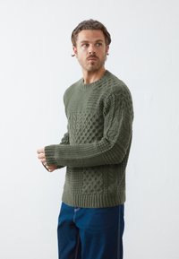 Strikket sweater i olivengrøn med strukturerede mønstre, ribbede manchetter og kant. Lange ærmer og rund hals med en afslappet pasform.