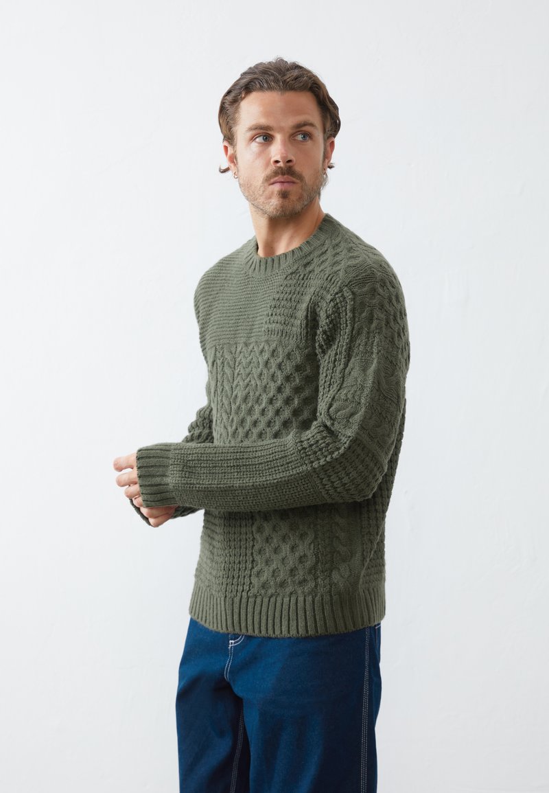 Strikket sweater i olivengrøn med strukturerede mønstre, ribbede manchetter og kant. Lange ærmer og rund hals med en afslappet pasform.