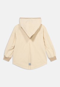 Μπεζ μπουφάν με κουκούλα και μακριά μανίκια, με ριμπ μανσέτες και μια πιέτα στο κέντρο της πλάτης, εμφανιζόμενο από πίσω σε λευκό φόντο.