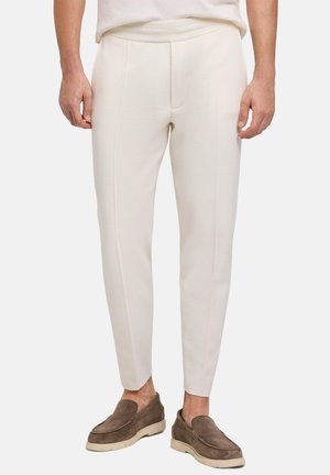 Witte, slim-fit broeken met een gladde textuur en voorplooien, gecombineerd met bruine loafers met een zachte suède afwerking en lichte zolen.