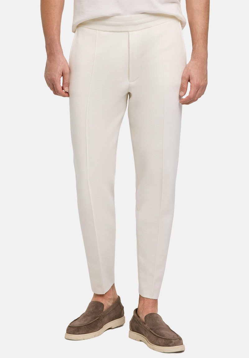Witte, slim-fit broeken met een gladde textuur en voorplooien, gecombineerd met bruine loafers met een zachte suède afwerking en lichte zolen.