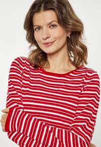 Tricou cu mâneci lungi, în dungi roșii și albe, cu un decolteu rotund și o textură moale, strâns pe încheieturi.