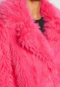 Różowy płaszcz z futra sztucznego o grubej, puszystej teksturze. Posiada szeroki kołnierz i luźny krój, podkreślający ciepło i komfort.