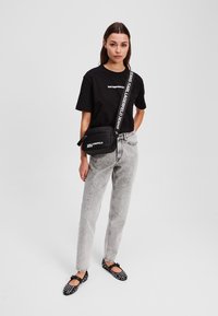 T-shirt nera con testo bianco, jeans grigi chiari, borsa a tracolla nera con logo bianco e ballerine nere a pois con fiocchi.