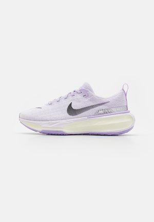 Lichtpaarse Nike hardloopschoen met zwart Swoosh-logo, mesh bovenwerk, dikke witte gedempte zool en trekhaak bij de hiel.