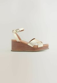 Sandales compensées métalliques dorées avec un design à lanières croisées. Équipées d'un talon en bois et d'une bride de cheville réglable pour un maintien sécurisé.