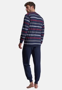 Langes Oberteil in Marine- und Graustreifen mit gerippten Bündchen, kombiniert mit einfarbigen Marine-Jogginghosen. Weicher Stoff mit lockerer Passform, barfuß getragen.