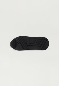 Schwarze Gummisohle mit einer strukturierten Oberfläche, die horizontale und diagonale Rillen für besseren Halt aufweist. Das Design ist flach mit abgerundeten Kanten.