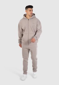 Lichtgrijze zip-up hoodie en bijpassende joggingsbroek gemaakt van zachte stof. De hoodie heeft een kangoeroezak en ribgebreide manchetten.