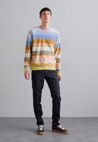 Sweatshirt listrado multicolor em tons pastel, em mistura de algodão, com gola redonda, punhos canelados, combinado com jeans de lavagem escura e ténis castanhos.